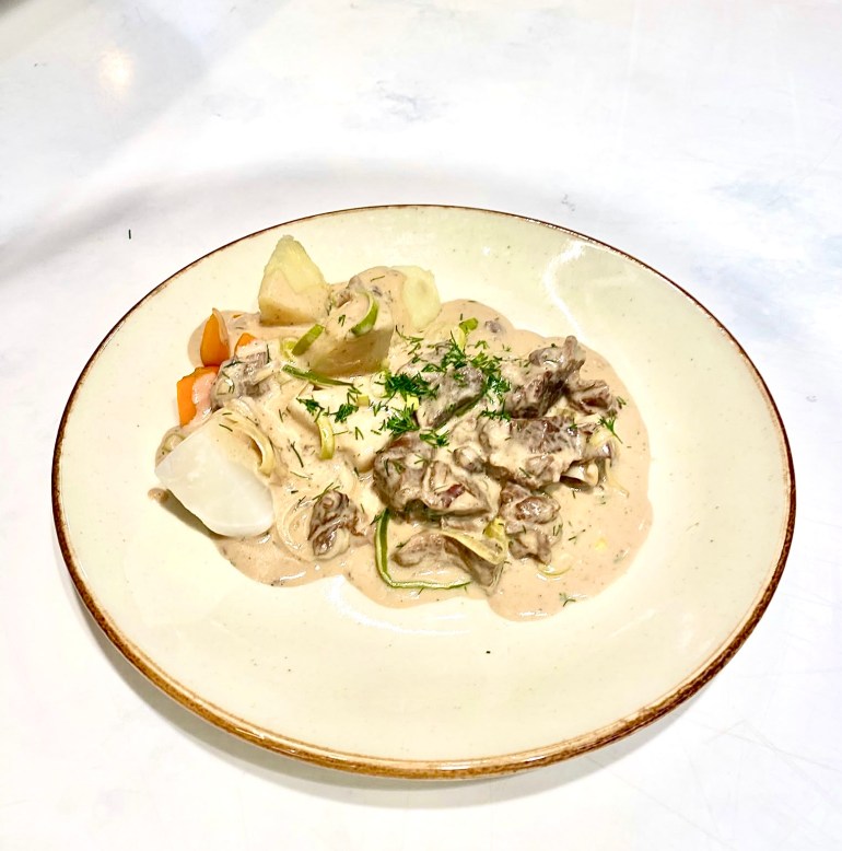 En tallerken med kremet gryterett servert med grønnsaker som gulrot, potet og kålrot, pyntet med dill.